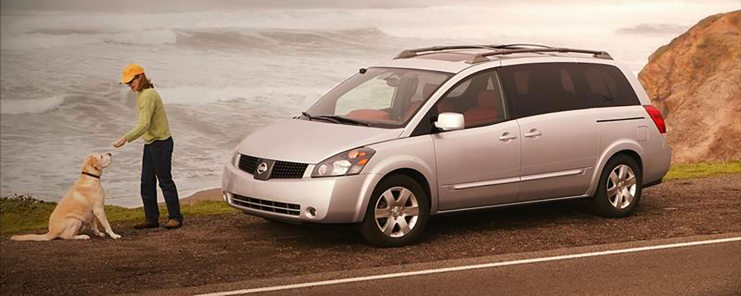 A Nissan Quest parked along a cliff with a person and a dog