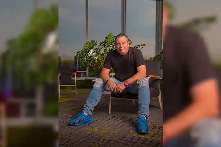 Guy Rodríguez de camiseta preta, calça jeans e tênis azul sentado em uma poltrona