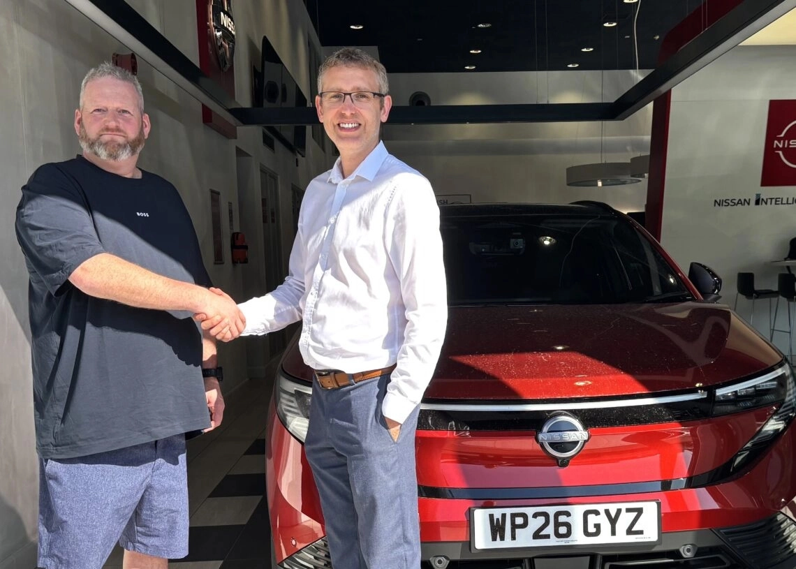 Two people shaking hands in a Nissan showroom beside a red Nissan LEAF