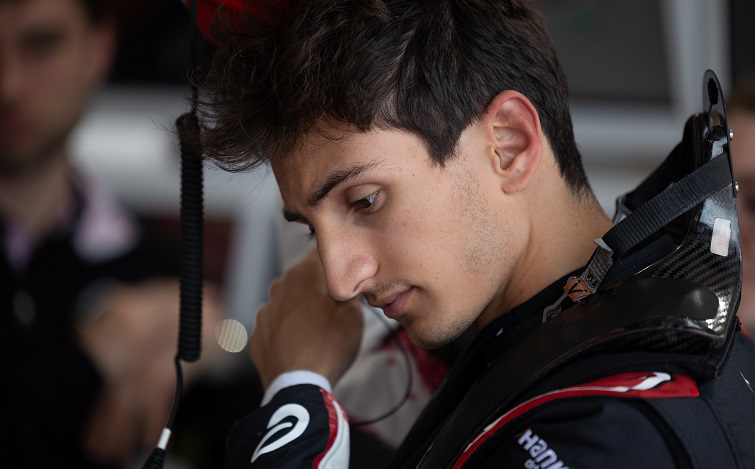 Gabriele Minì preparing himself for the session with his HANS device attached and putting in his earpieces into his right ear (not visible).