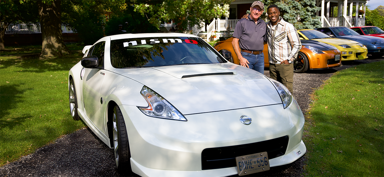 Two people facing forward smiling next to white car