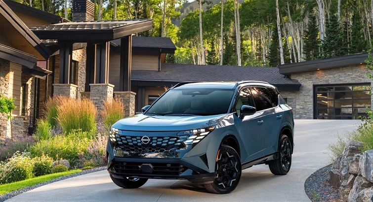 Front left 3/4 angle of the 2027 Nissan Rogue Hybrid Platinum parked in front of a house with trees behind.