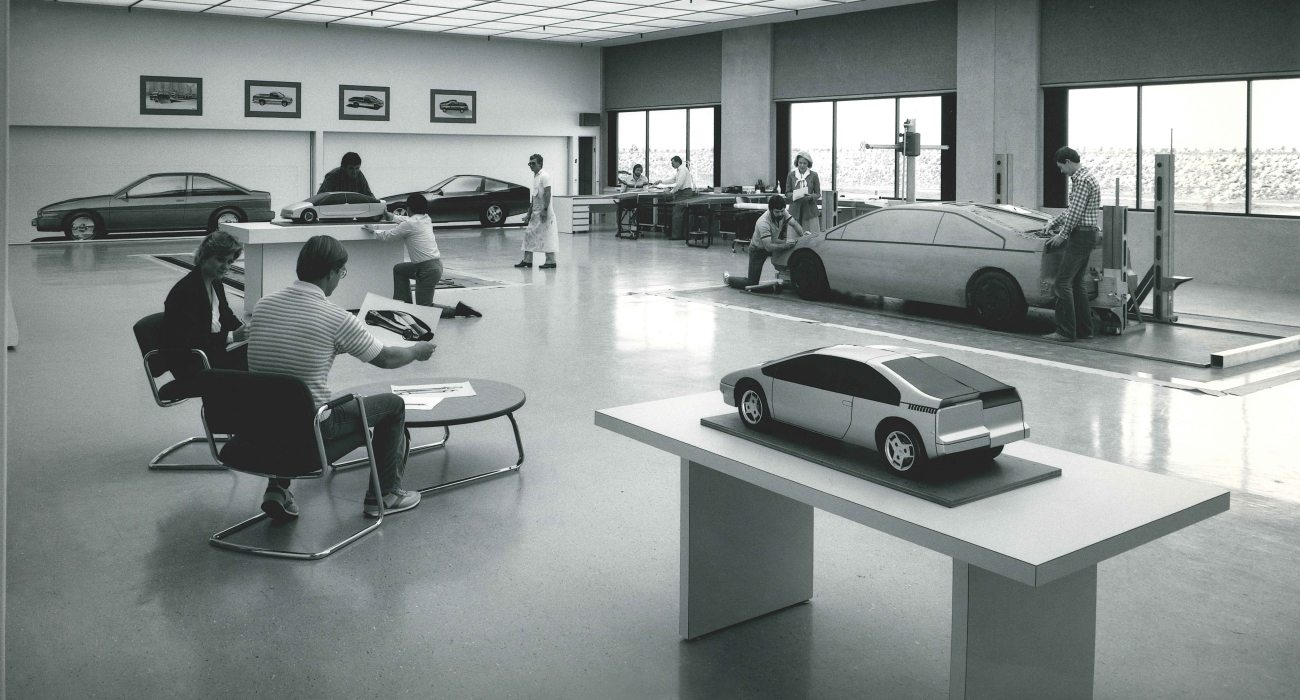 Black and white photo of serveral people in a room with model cars and images