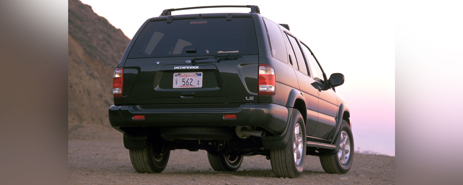 A black Nissan Pathfinder parked on a dirt road with a mountain seen on the background.