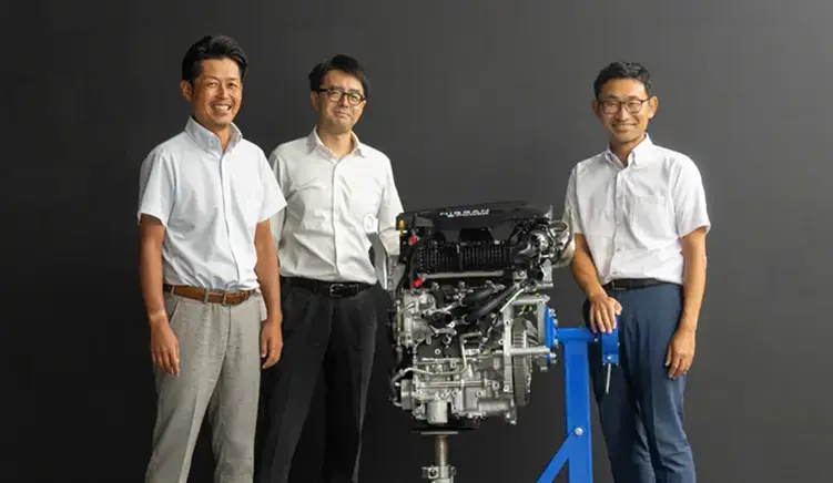 A group of Nissan employees standing next to a car engine.