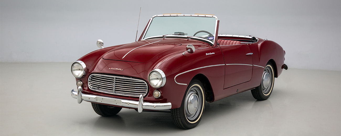 A red Datsun Fairlady 1200 Roadster parked in a white room.