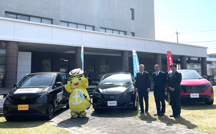電気自動車（サクラ、リーフ、アリア）の前で記念撮影する各代表者（男性３名とご当地キャラクター）