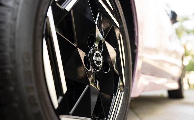 Close-up of a Nissan car's aluminum wheels (tires). Green seedlings in the background.