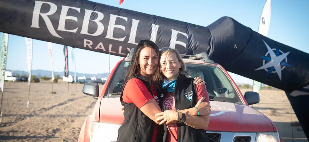 2 people hugging each other in front of a red Nissan truck.