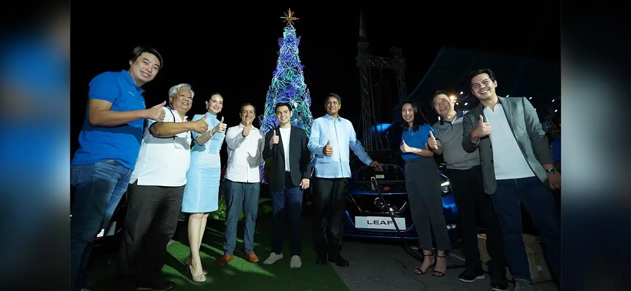 A group of people standing with the Nissan LEAF and giant Christmas Tree at their back