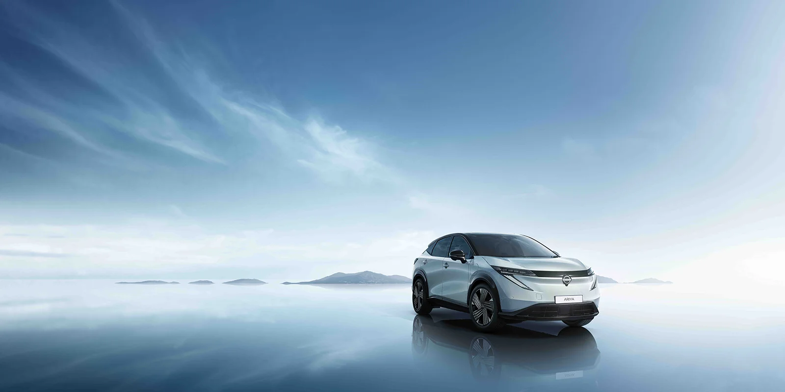 Vue de profil à droite de la Nissan ARIYA 2027 garée sous un ciel bleu, avec une chaîne de montagnes en arrière-plan