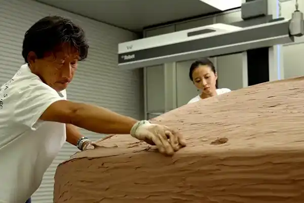 2 people working on a clay sculpture.