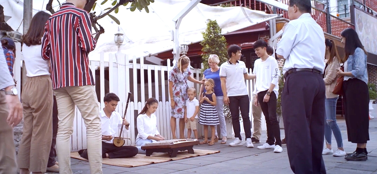 2 people playing musical instruments sitting on the ground while a group of people surrounding them.