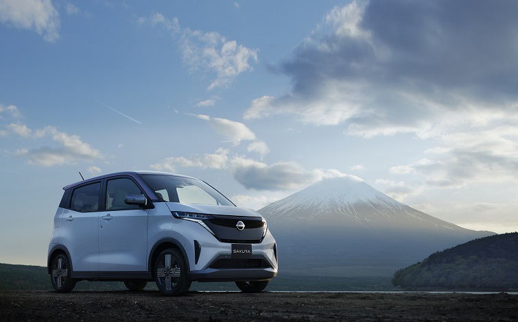 夜明けの静謐な空の下、遠く富士山を望んで停車する白い「日産サクラ」
