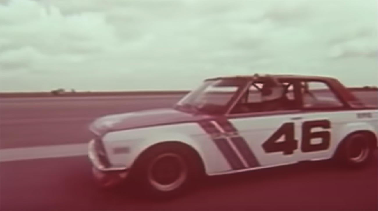 A black and white image of a Datsun driving on a road.