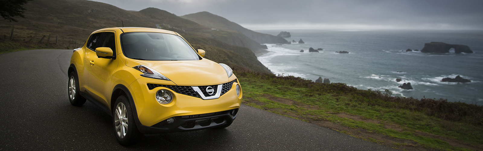 A yellow Nissan Juke driving around a curved road with the ocean to the right.