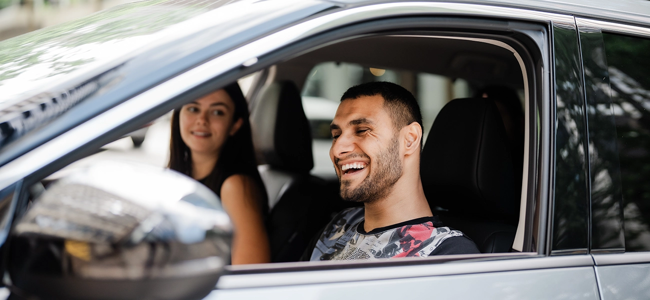 Emmanuel Kelly sitting in the front of a blue car smiling and looking out the window