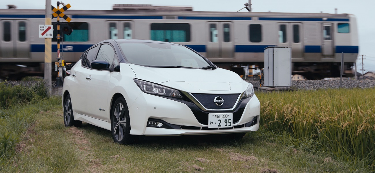 Un automóvil Nissan blanco estacionado frente a un tren en movimiento.