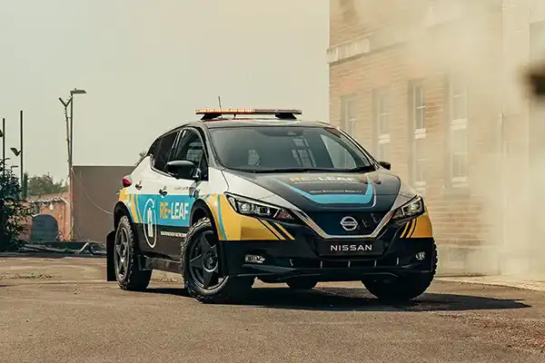 A Nissan LEAF parked next to a smokey building.