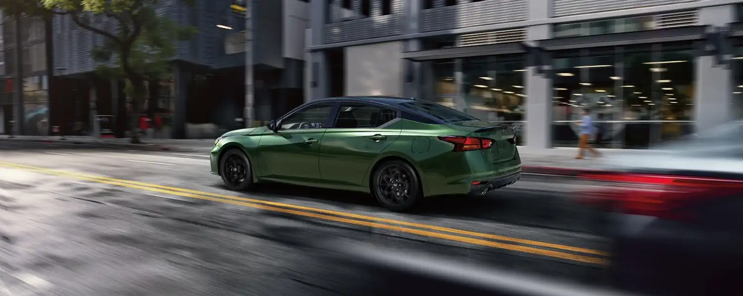 A green Nissan Altima driving on a busy street