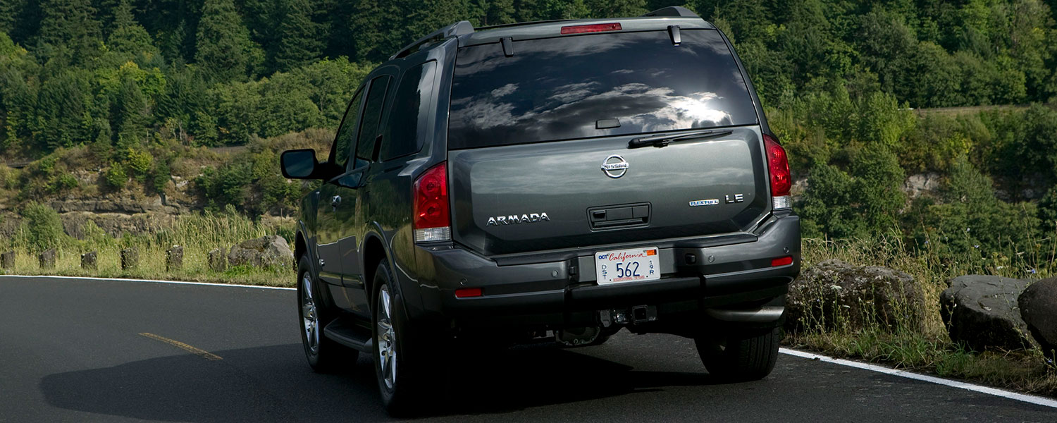 A Nissan Armada driving on a road near green forest background