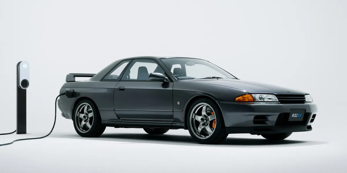 A Nissan GT-R plugged into an EV charger in front of a grey background