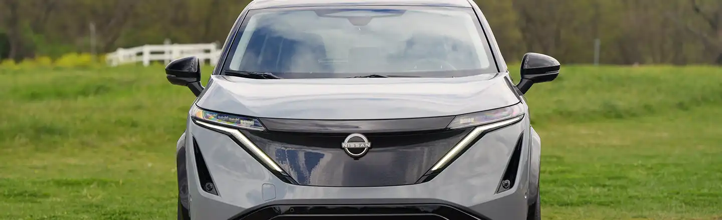 Front view of a grey 2024 Nissan ARIYA with greenery in the background