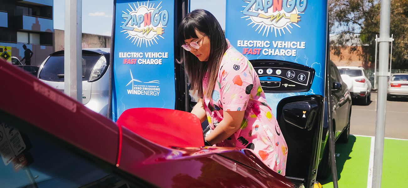 Lisy Kane in a pink jumpsuit charging her red Nissan LEAF