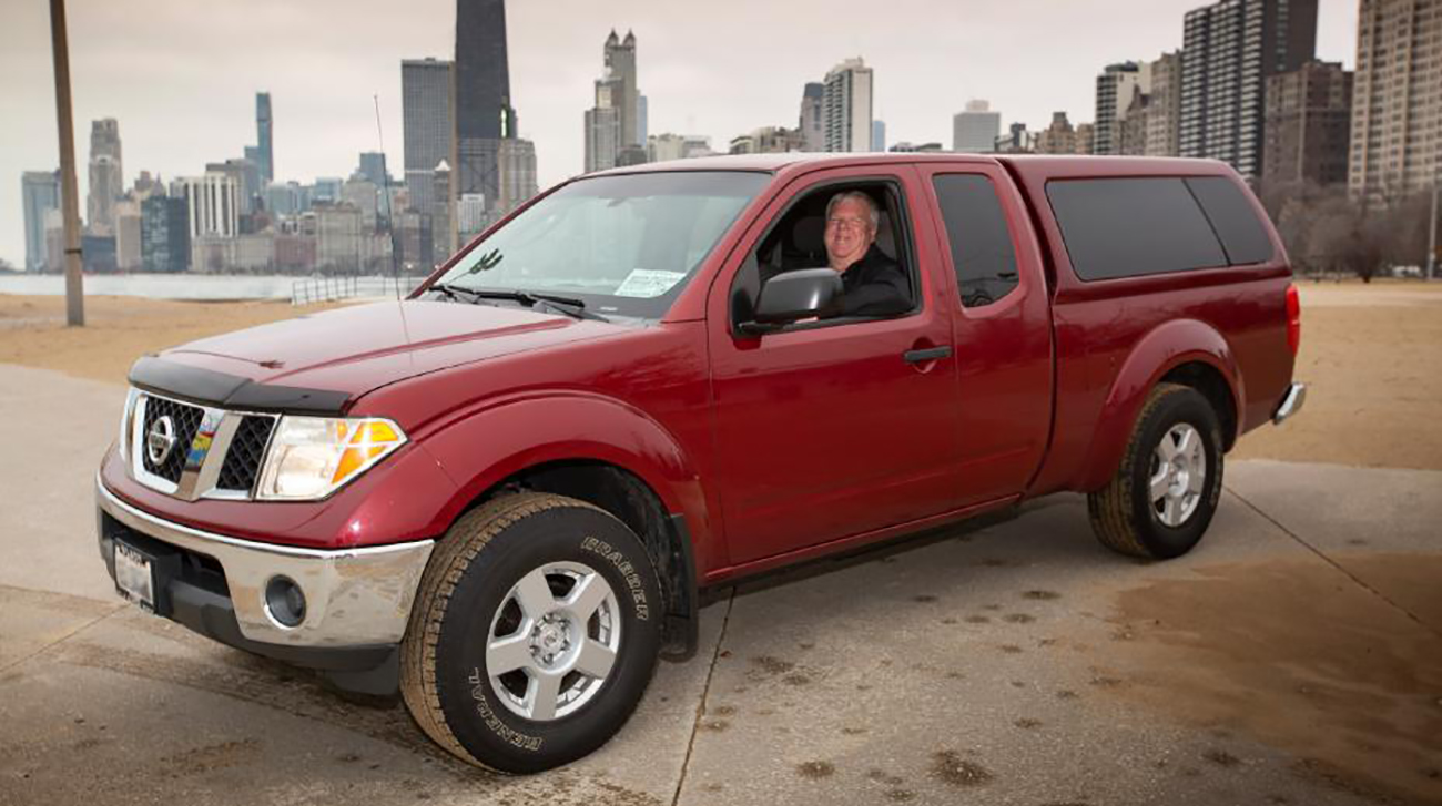 A red Frontier King Cab pickup parked in a park with Brian Murphy in the driver seat.
