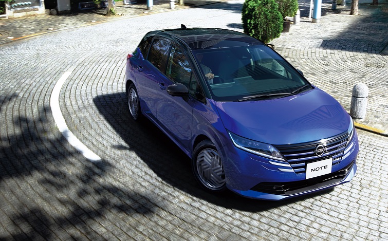石畳を画面手前側にカーブして走る日産ノート（スミレ スーパー���ラック 2トーン）