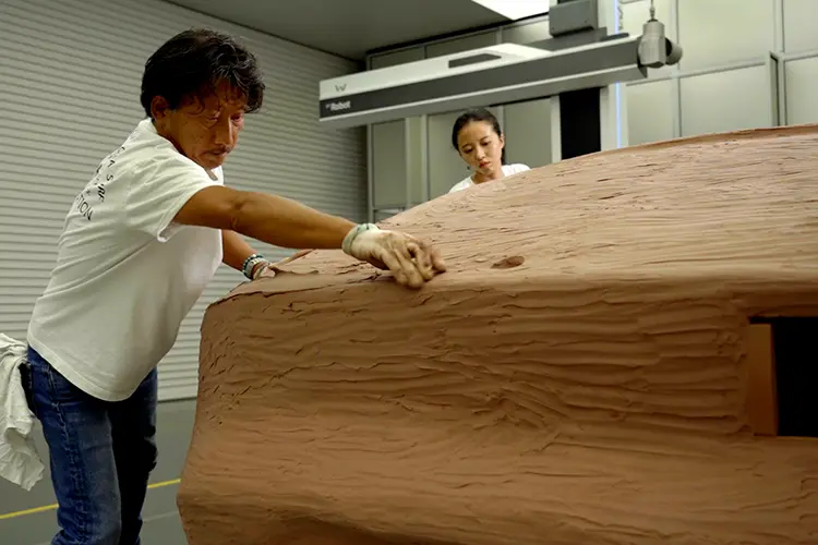 Close up of two people working on a clay model of vehicle