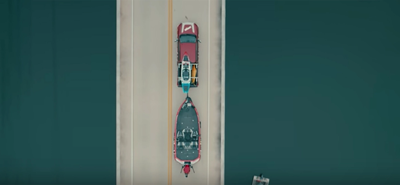 Nissan Titan with a boat attached to the back of the car driving on a bridge.