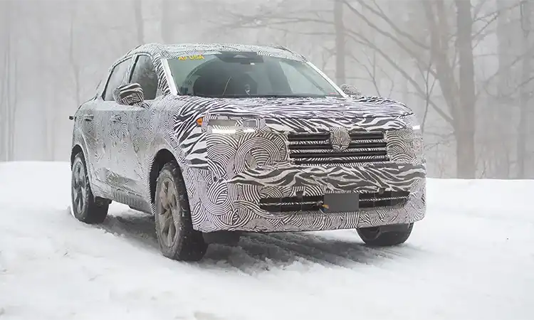 A white camouflaged 2025 Nissan Kicks driving along a snowy path in the woods.