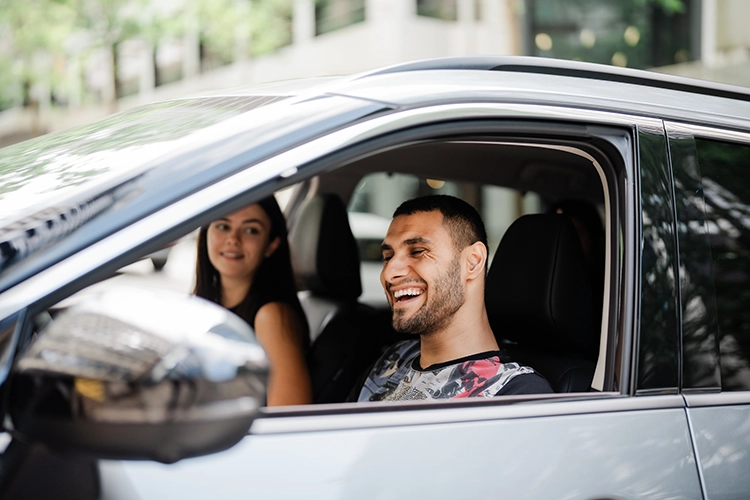 Emmanuel Kelly sitting in the front of a blue car smiling and looking out the window