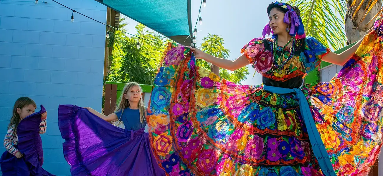 A dancing woman in a colorful dress with the sun shining through the colors with two children on her side