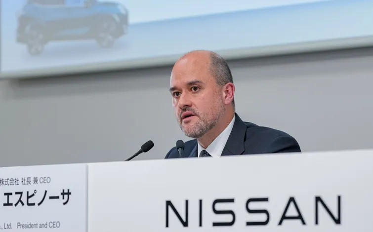 日産CEO イヴァン エスピノーサが会見で発言する様子。白い背景に車両画像が映り、前方には「NISSAN」と書かれたパネルとマイクが配置されている。スーツ姿で正面を向いている。
