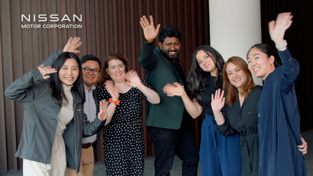 Seven people facing forward and smiling and waving