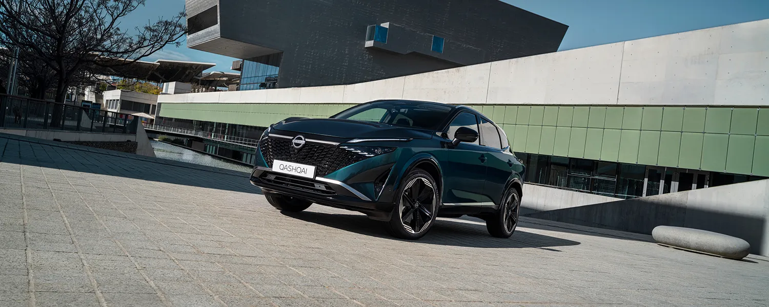 Nissan Qashqai parked in front of a modern architectural building, shown from a front three-quarter angle