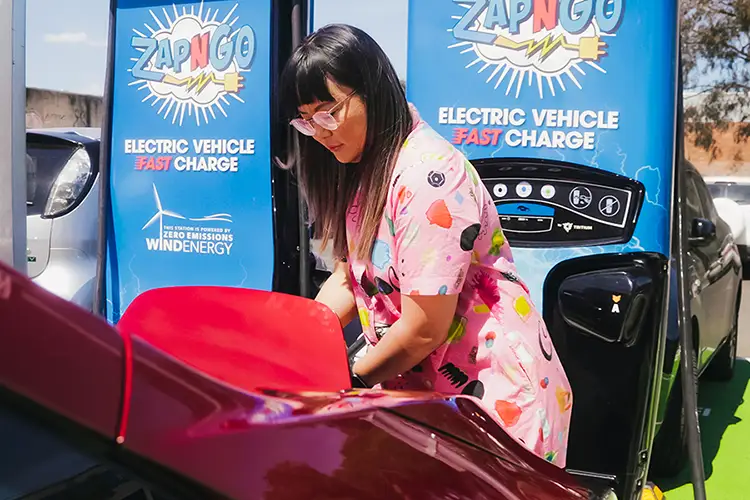 Lisy Kane in a pink jumpsuit charging her red Nissan LEAF