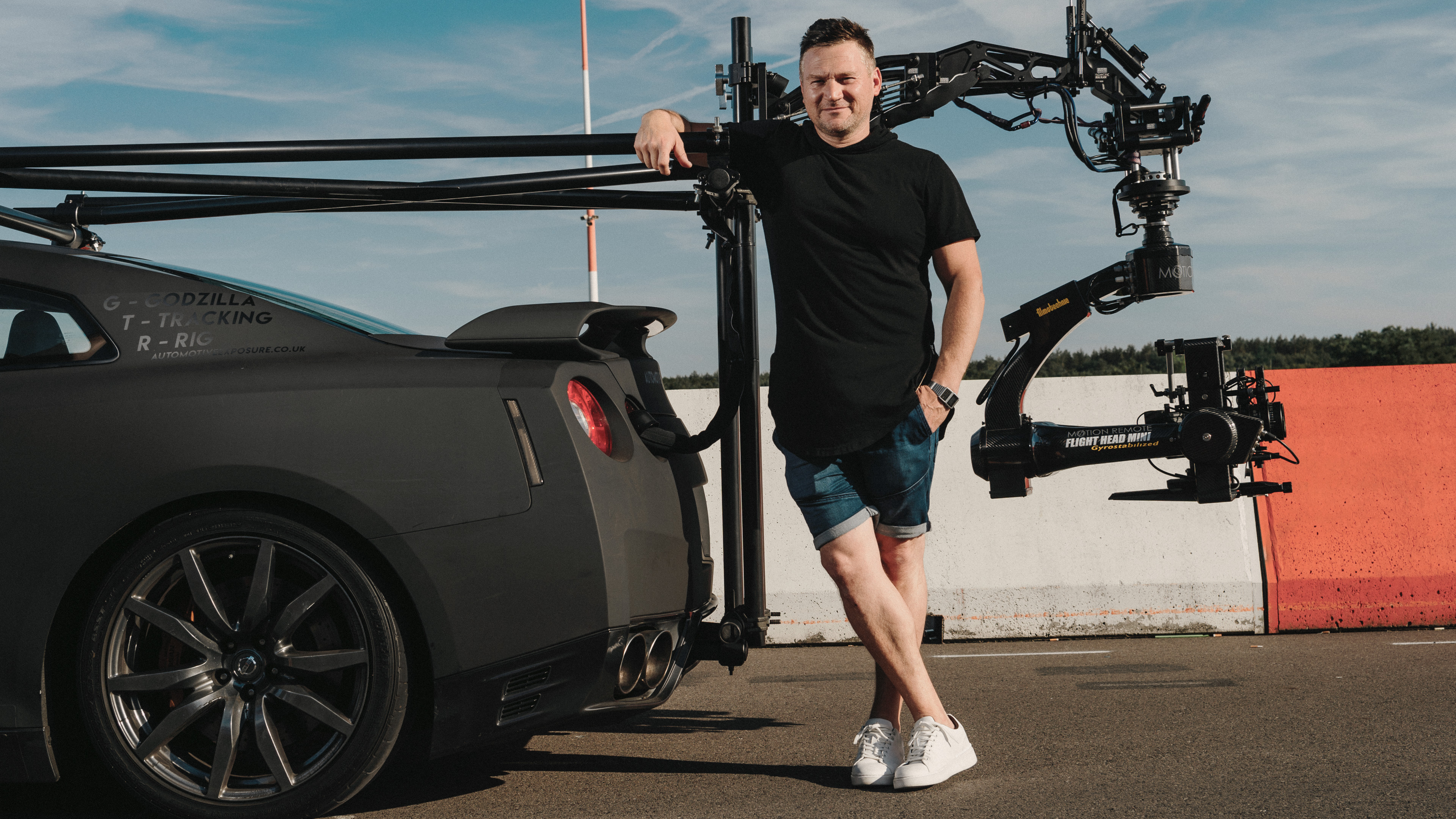 A man standing at the back of dark gray Nissan GT-R.
