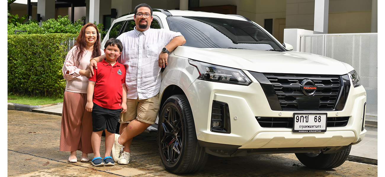 Two adults and one child smile and stand next to a white vehicle