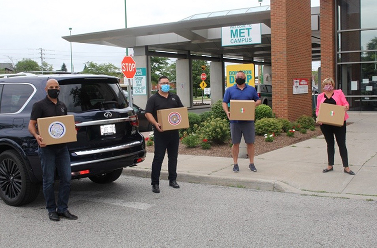 Four people wearing medical masks holding boxes of meals outside of hospital