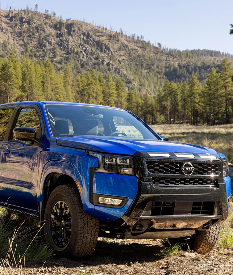 Front right 3/4 view of the 2027 Nissan Frontier Sport Edition parked on a clearing in a wooded area.