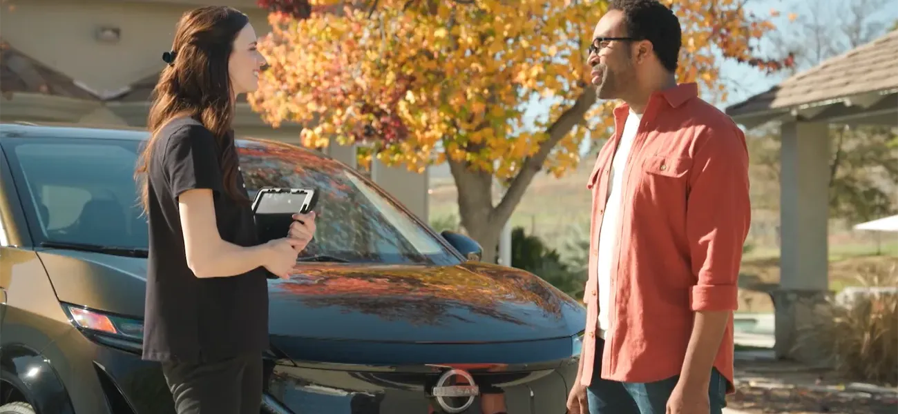 A woman and man chatting in front of a black Nissan Ariya during fall time.