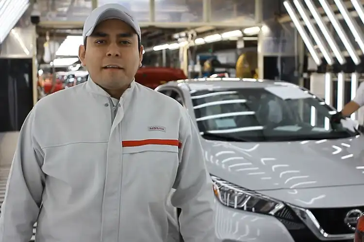 Un hombre posando para una foto en una planta de producción de vehículos.