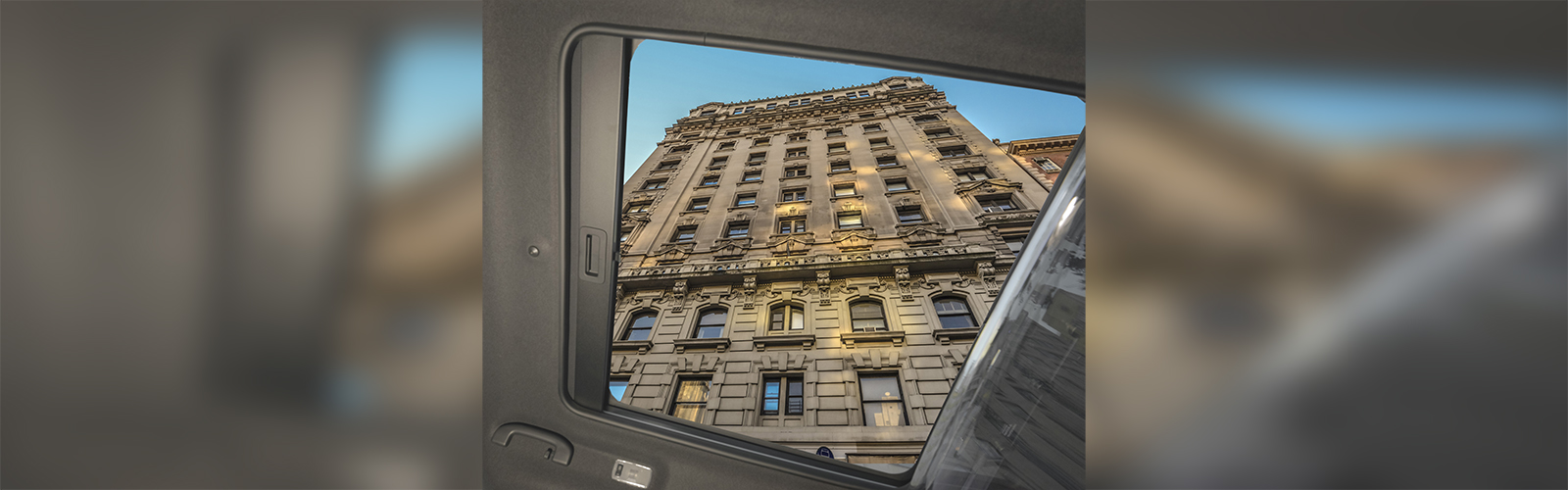 The view from inside of a Nissan NV200 looking up at a tall building through an open sunroof.