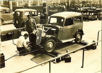 Una antigua fotografía en blanco y negro que muestra a dos personas trabajando en un automóvil.