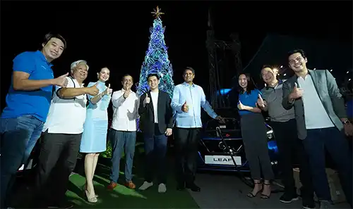 A group of people standing with the Nissan LEAF and giant Christmas Tree at their back