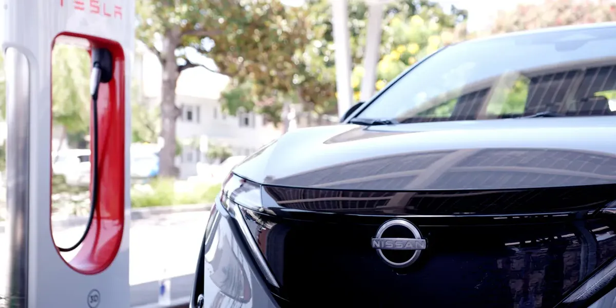 Close up of 3 /4 of a grey 2025 Nissan ARIYA in front of a Tesla charger