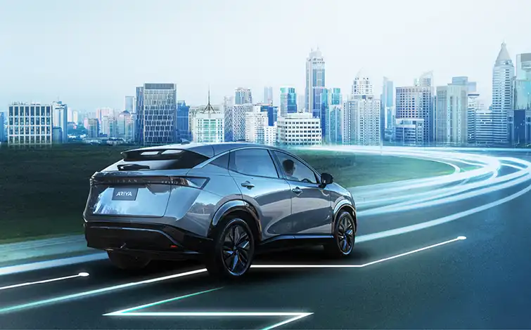 Image of a Nissan Ariya driving towards a big city with tall buildings, with illumination on the road